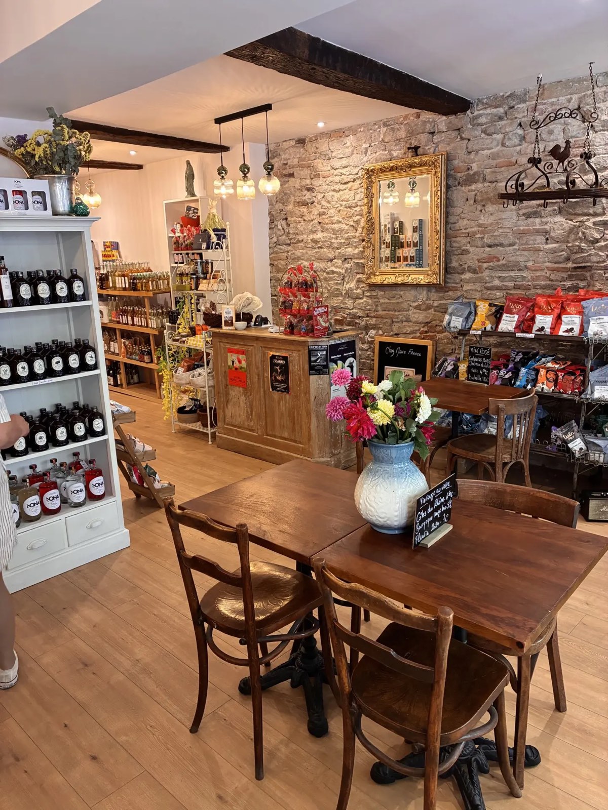 Intérieur chaleureux de Chez Marie France : tables en bois, fleurs fraîches et mur de pierres